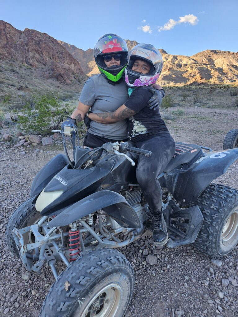 Two people on an ATV tour near Las Vegas, Nevada, smile together in helmets amidst desert mountains and rocky terrain.