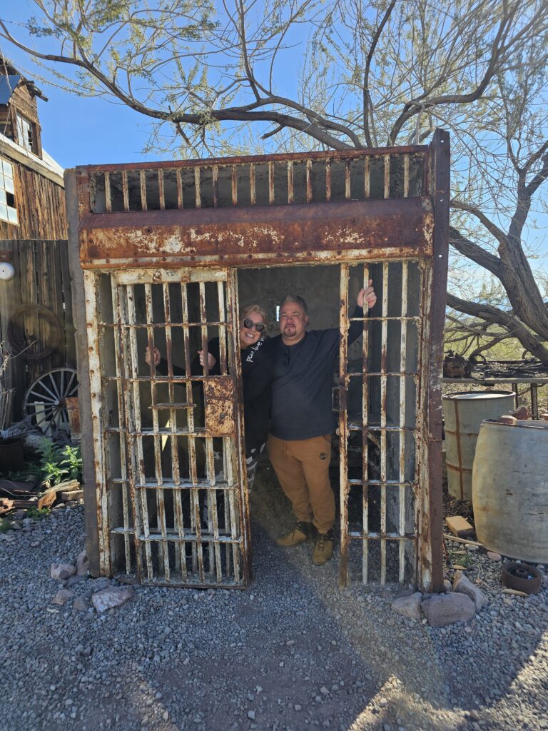 Two visitors pose playfully in a rustic jail cell at a Nevada ghost town near the Colorado River, ideal for Las Vegas sightseeing tours.