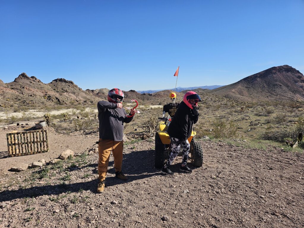 Two helmeted riders by a yellow ATV in Nevada desert near Las Vegas, enjoying an off-road RZR tour adventure.