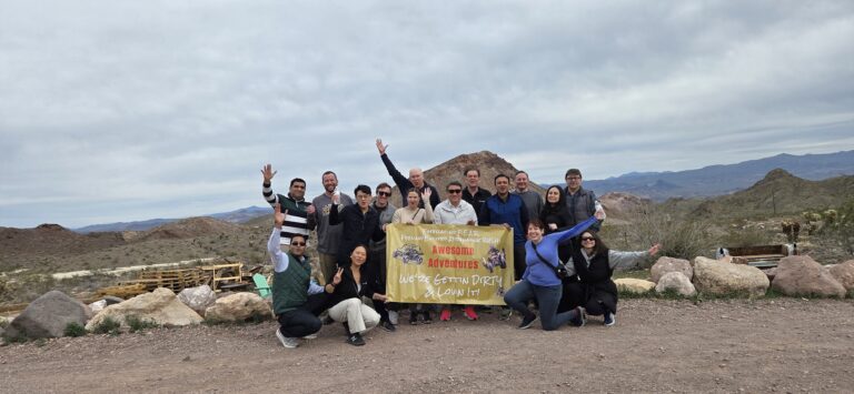 Smiling group in Nevada poses by rocky terrain with “Awesome Adventures” banner after ATV tour near Las Vegas and Colorado River.