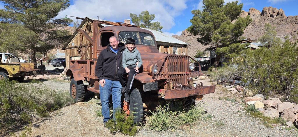 Smiling man and child by a rusted truck in a Nevada ghost town near Las Vegas, perfect for sightseeing and ATV tours.