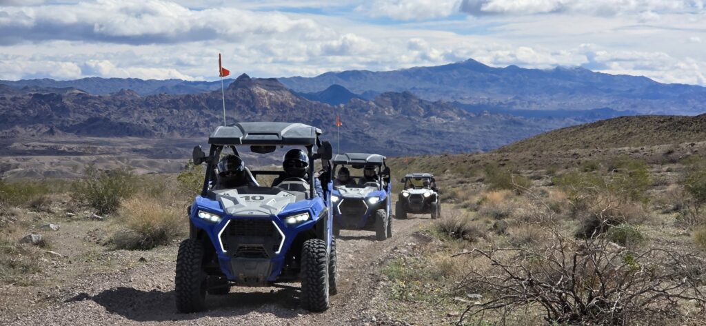 ATVs with orange flags drive single file on a rocky Nevada trail near Las Vegas, perfect for RZR off-road tours and sightseeing.