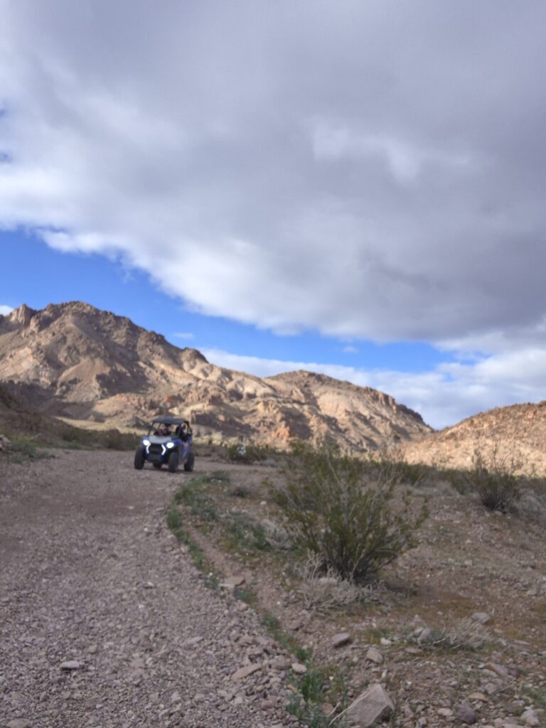 An ATV powers across a rocky desert trail near Las Vegas, Nevada, with rugged mountains and clouds in the backdrop.
