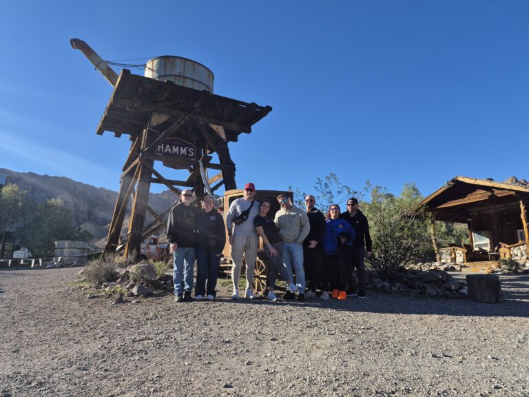 Seven people stand by a wooden HAMMS water tower near a rustic Nevada ghost town, perfect for ATV tours and Colorado River views.
