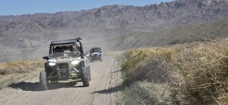 ATVs kick up dust on a Nevada trail near Las Vegas, with rugged hills and blue sky—perfect for RZR off-road adventure tours.
