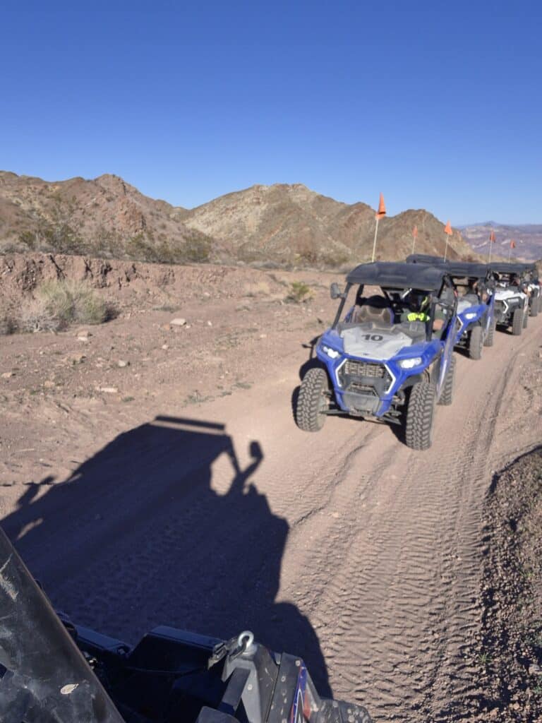 Blue off-road ATVs with orange flags ride a dusty Nevada desert trail near Las Vegas, perfect for scenic RZR tours.