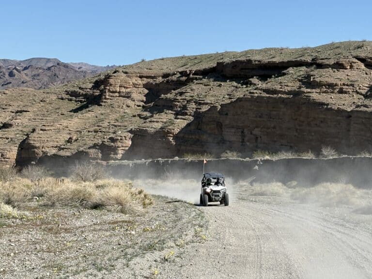 RZR off-road vehicle tours a dusty Nevada desert trail near Las Vegas, with rocky hills and sparse vegetation under blue skies.