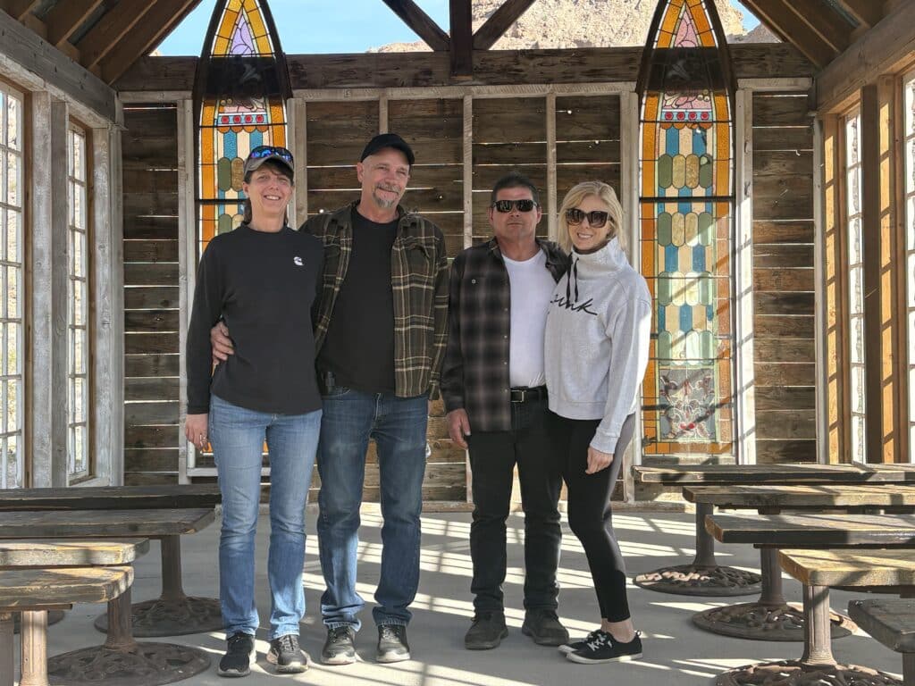 Smiling adults in a rustic Las Vegas ghost town building with stained-glass windows—perfect for sightseeing or ATV tours nearby.