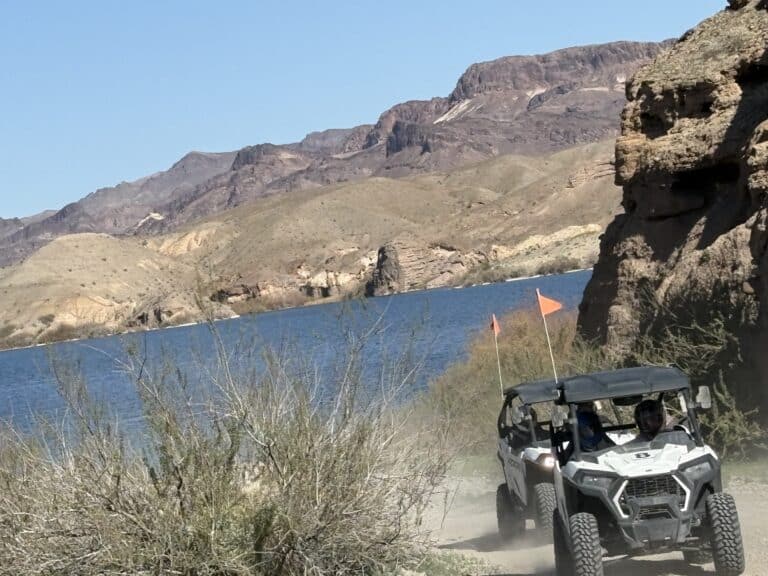 Adventurers enjoy an RZR off-road ride near the Colorado River by Las Vegas, with orange flags waving in Nevada’s desert landscape.