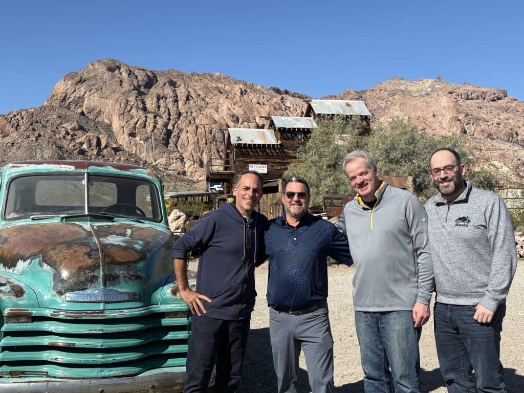 Four men smile by a vintage turquoise truck in a Nevada ghost town, great for Las Vegas ATV tours and Colorado River adventures.