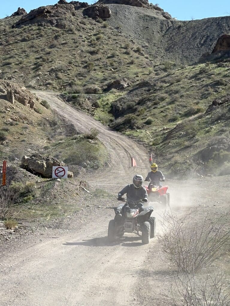 ATV riders explore a dusty Nevada trail near Las Vegas, passing a no-entry sign on scenic off-road RZR tour terrain.