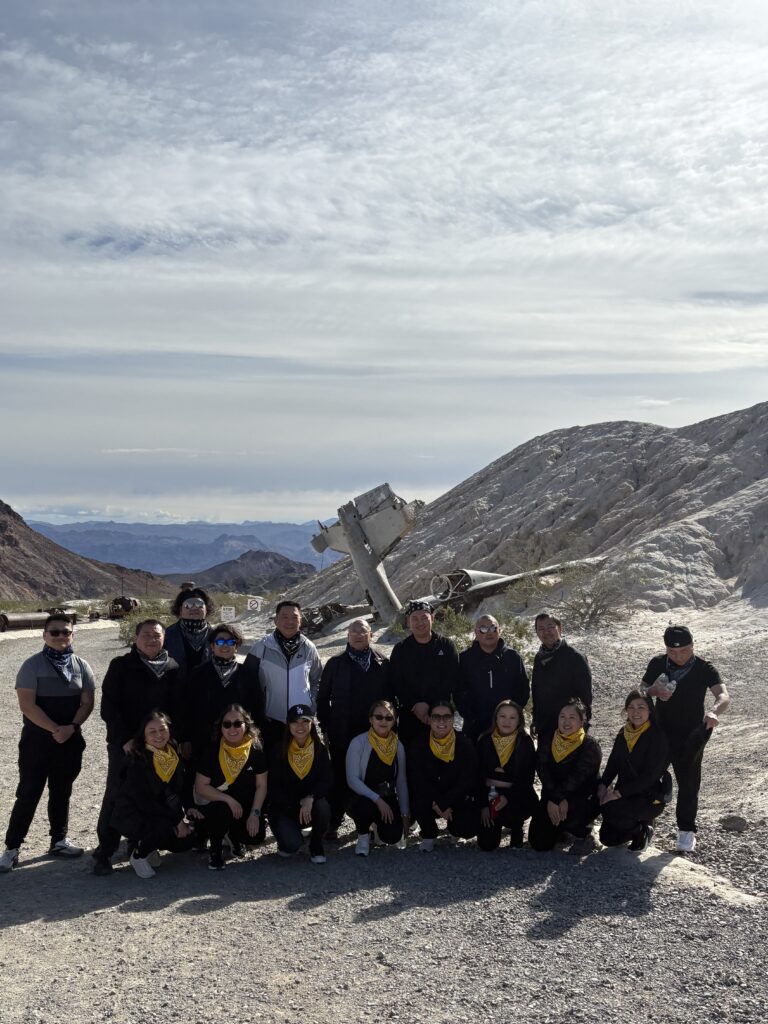 Group posing by rocky Nevada landscape near a crashed plane, with yellow scarves—Las Vegas ATV or RZR tour adventure.