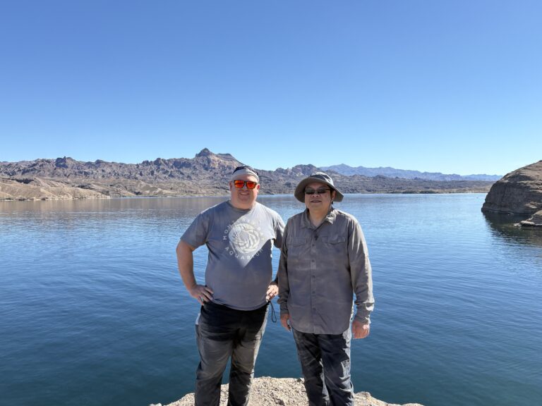 Two people in hats stand on a rocky Nevada shore by the Colorado River near Las Vegas, ready for outdoor ATV and ghost town tours.