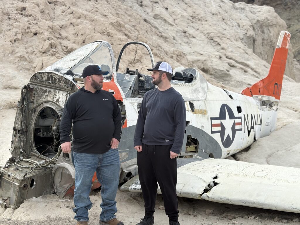 Two men in hats talk near a Navy aircraft wreck on a Nevada desert tour, ideal for ATV or RZR rides near Las Vegas.