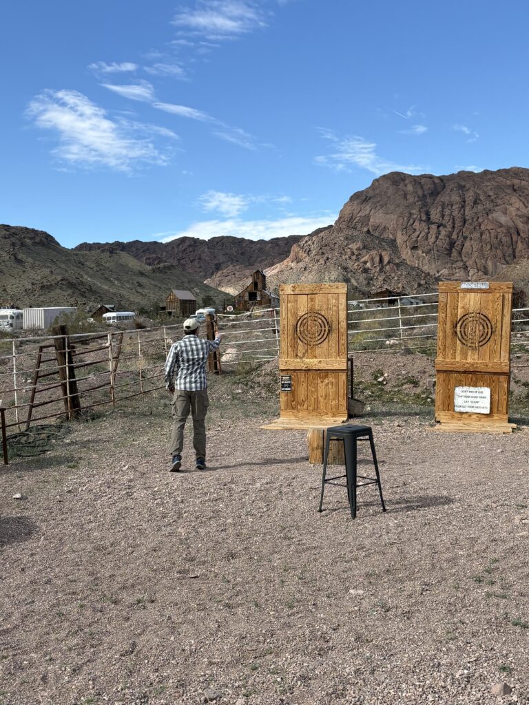 A person by wooden axe-throwing targets in a Nevada desert near Las Vegas, with mountains and Ghost Town sightseeing views.