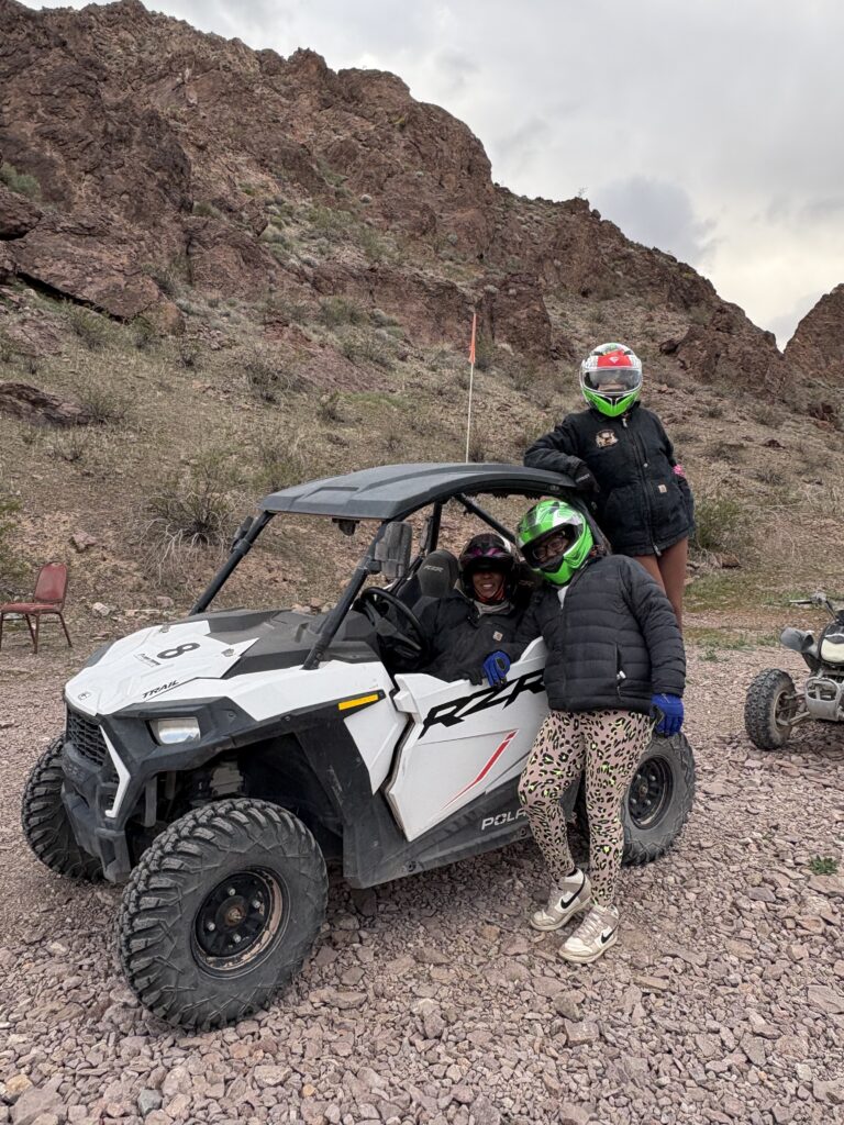 Adventurers in helmets by a white RZR on rocky Nevada terrain near Las Vegas, ready for an ATV off-road tour.