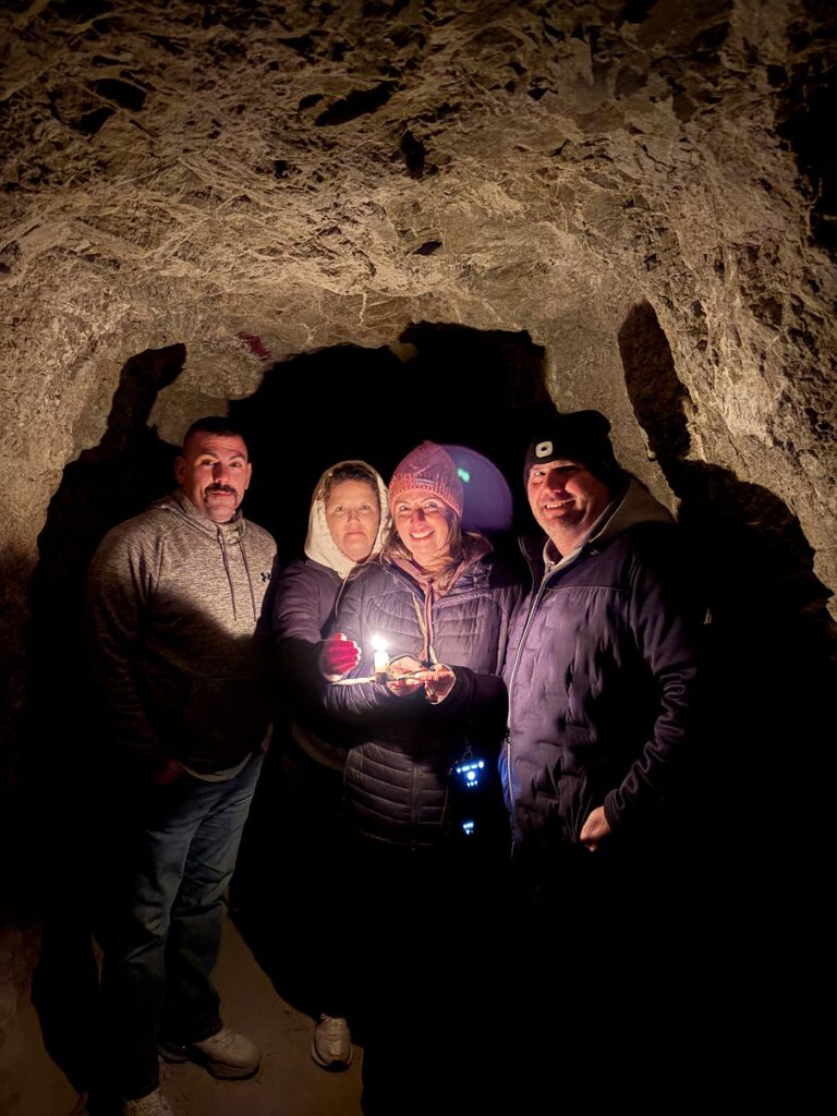 Adventurers in warm gear explore a dark Nevada cave near the Colorado River, lit by candlelight after an ATV tour.