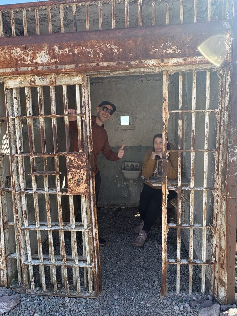 Couple poses playfully by a rusty jail cell at a Nevada ghost town, perfect for Las Vegas ATV tours and Colorado River sightseeing.