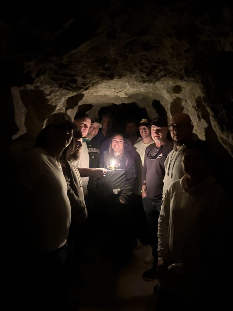 Visitors gathered in a dim Nevada cave near Las Vegas, faces lit by candlelight during a Colorado River Ghost Town tour.