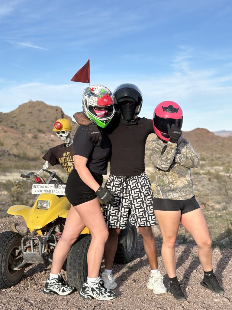 Group in helmets by yellow ATV poses in Nevada desert near Las Vegas, ready for an exciting ATV tour under blue skies.