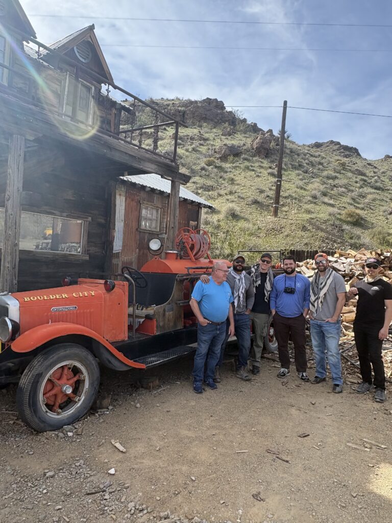 Six men by a vintage Boulder City fire truck in Nevada, near Las Vegas and Colorado River, perfect for Ghost Town sightseeing.