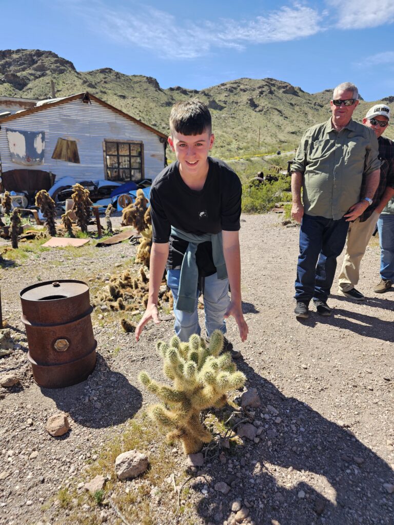 Smiling boy by a cactus in a Nevada ghost town near Las Vegas, with adults nearby; perfect for ATV tours and sightseeing.