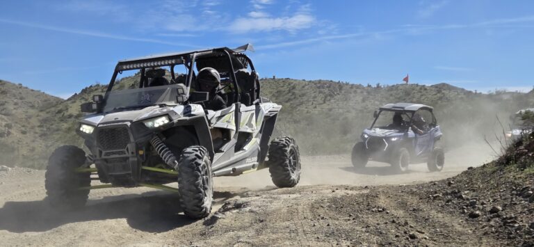 ATV tour near Las Vegas: two off-road vehicles speed on dusty Nevada trails, desert hills and clear blue sky in the background.
