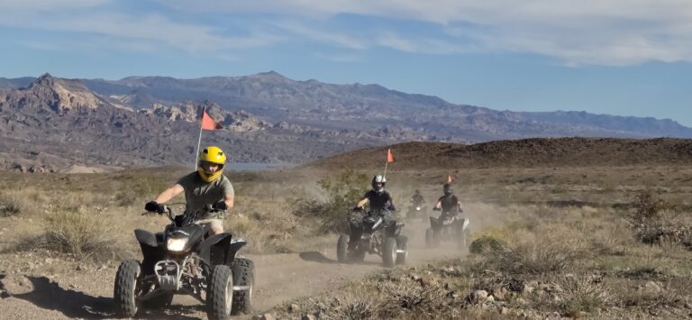 Adventurers enjoy an ATV tour near Las Vegas, Nevada, riding dusty trails with orange flags and rocky mountains in the background.