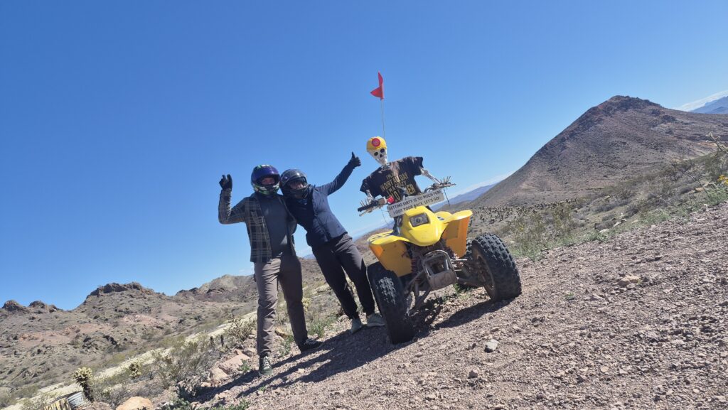 Two riders in helmets pose by a yellow ATV on a Nevada desert trail near Las Vegas, perfect for ATV tours and RZR off-road adventures.