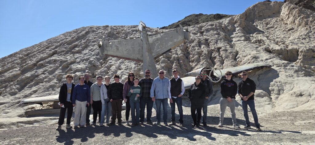 Group of 14 on Nevada desert terrain by a crashed plane near Las Vegas, perfect for ATV tours and Ghost Town sightseeing.