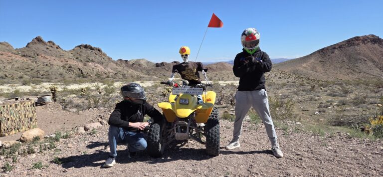 Adventurers in helmets pose by a yellow ATV and skeleton in Nevada desert near Las Vegas on an exciting ATV tour.