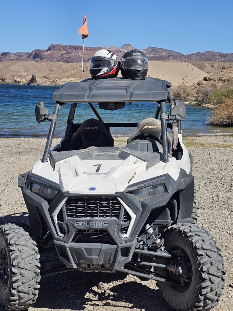 White Polaris RZR parked on rocky Nevada lakeshore, helmets on roof, perfect for Las Vegas ATV tours by the Colorado River.