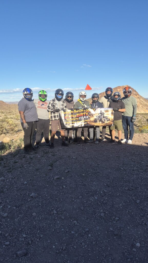 Group in helmets on rocky Nevada terrain near Las Vegas, holding "Live Bold Die Wild" banner during ATV RZR off-road tour.