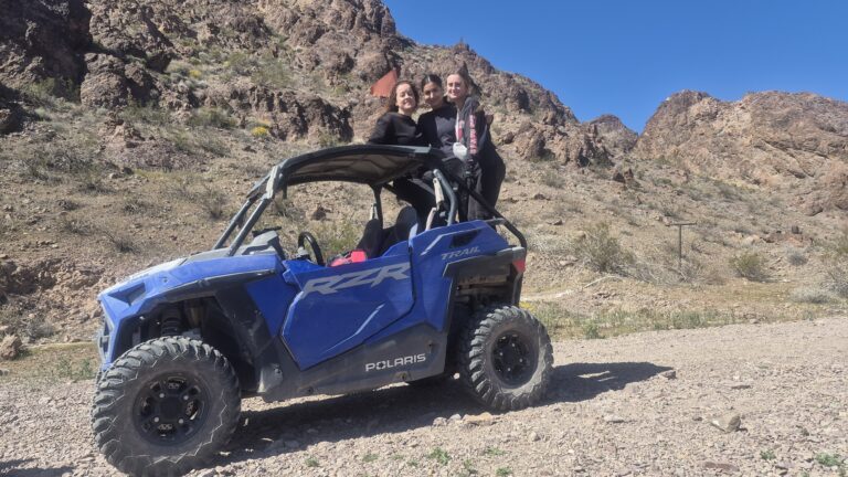Formalwear-clad pair smiles by blue Polaris RZR in Nevada desert near Las Vegas during an exciting ATV tour with mountain views.