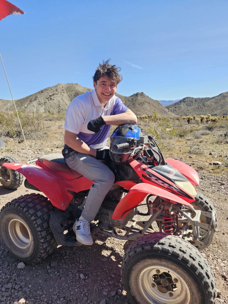 Smiling young man rides a red ATV in the Nevada desert near Las Vegas with mountains and clear skies—perfect for ATV tours.