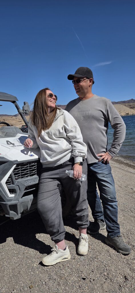 Smiling couple by gray off-road vehicle on Nevada beach near Colorado River, ideal for Las Vegas ATV tours and RZR adventures.