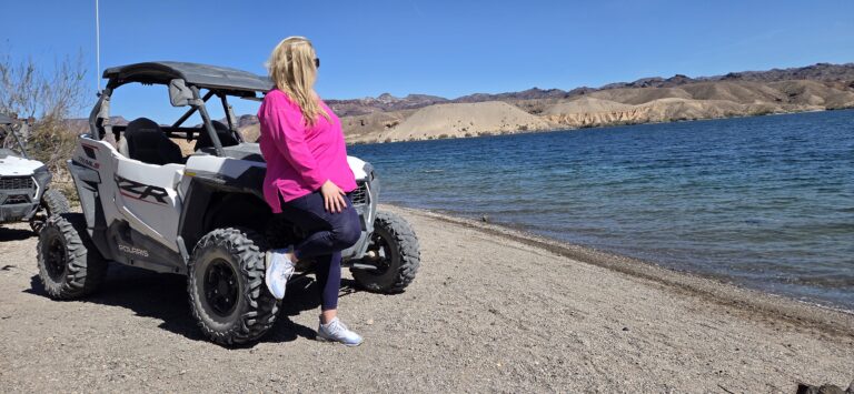 Woman in pink top and sunglasses by white off-road vehicle at Colorado River near Las Vegas, Nevada, enjoying RZR ATV ride.