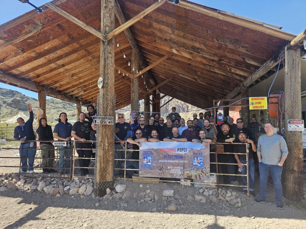 Smiling group under a rustic shelter in Nevada on an ATV tour near Las Vegas, rocky hills and Colorado River backdrop.