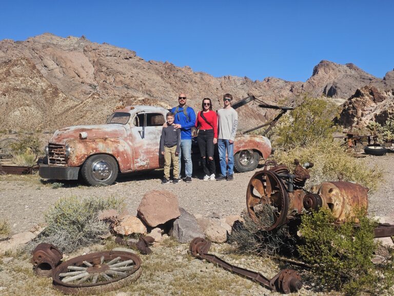 Family of four by a rusty old truck in Nevada desert near Las Vegas, perfect for Ghost Town sightseeing and ATV tours.