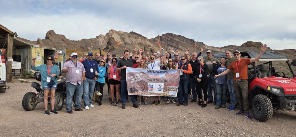 Smiling group in Nevada near Las Vegas with ATVs, holding Congratulations Team of the Quarter banner after an ATV tour.