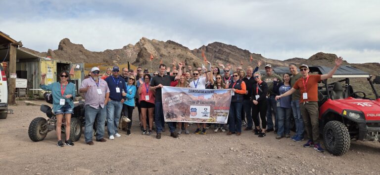 Smiling group in Nevada near Las Vegas with ATVs, holding Congratulations Team of the Quarter banner after an ATV tour.