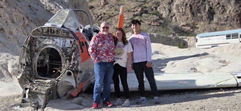 Three smiling people by a crashed plane and bus in Nevada desert near Las Vegas, perfect for Ghost Town sightseeing tours.