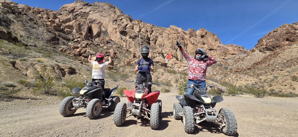 ATV riders with helmets and masks pose in the Nevada desert near Las Vegas, rocky formations behind; perfect for ATV tours.