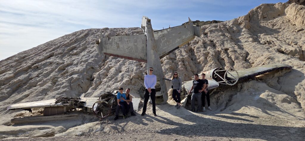 Group posing by a crashed airplane in Nevada’s desert near Las Vegas, perfect for ATV tours and Ghost Town sightseeing.