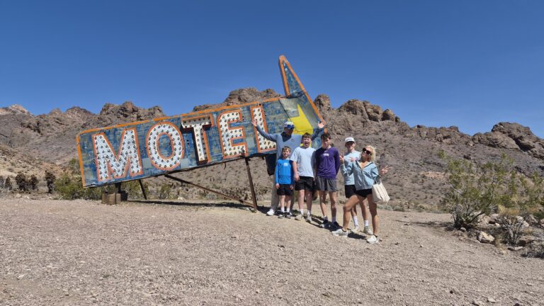 Six friends pose by a vintage Motel sign near the Nevada desert, perfect for Las Vegas ATV tours or Ghost Town sightseeing.