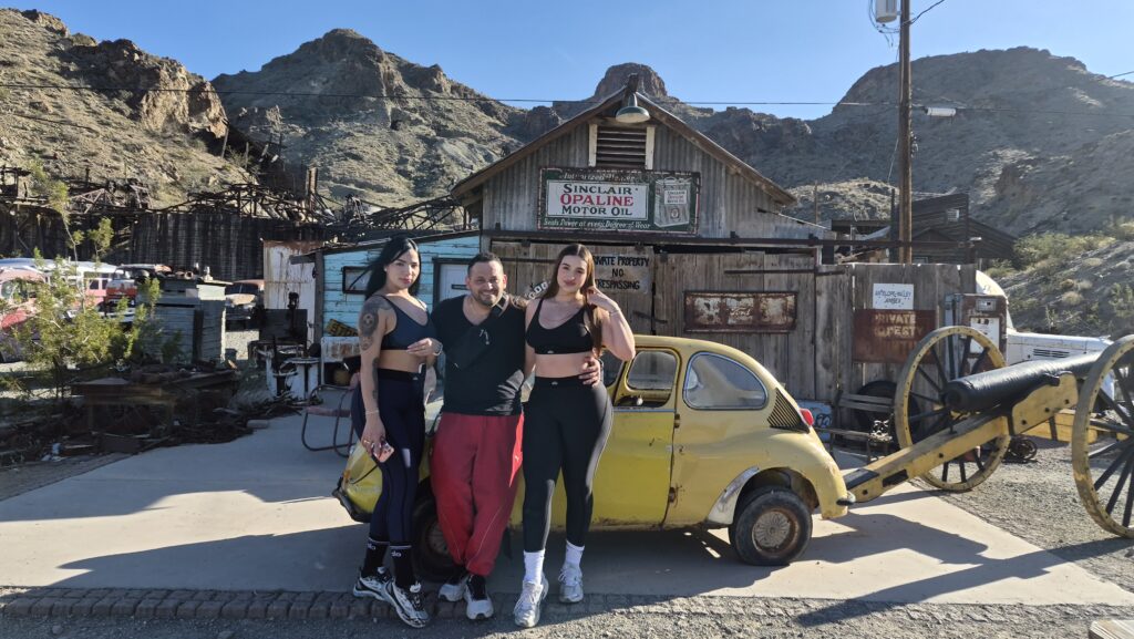 Smiling group at Nevada Ghost Town near Las Vegas, by vintage car and cannon, perfect for sightseeing or ATV tours.