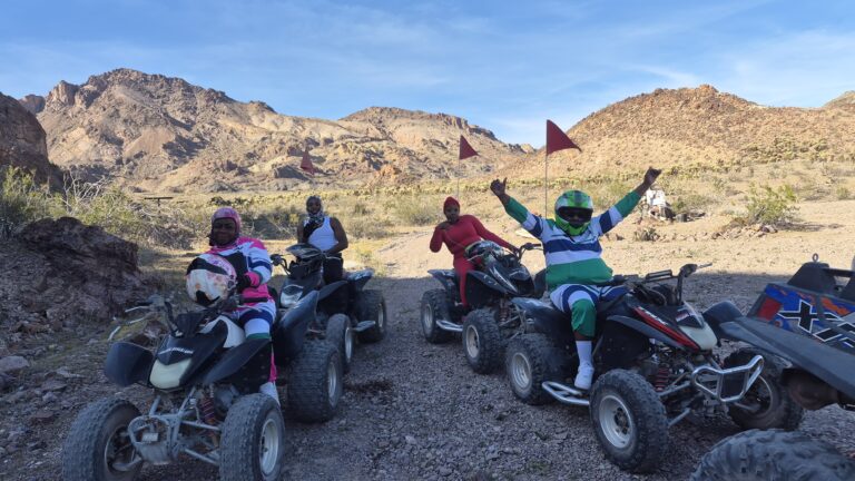 Riders in colorful gear on ATVs with red flags enjoy a Nevada desert trail near Las Vegas on an exciting ATV tour.