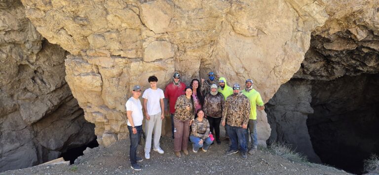 Twelve people pose by a Nevada cave near the Colorado River, ready for ATV tours or Ghost Town sightseeing in Las Vegas.