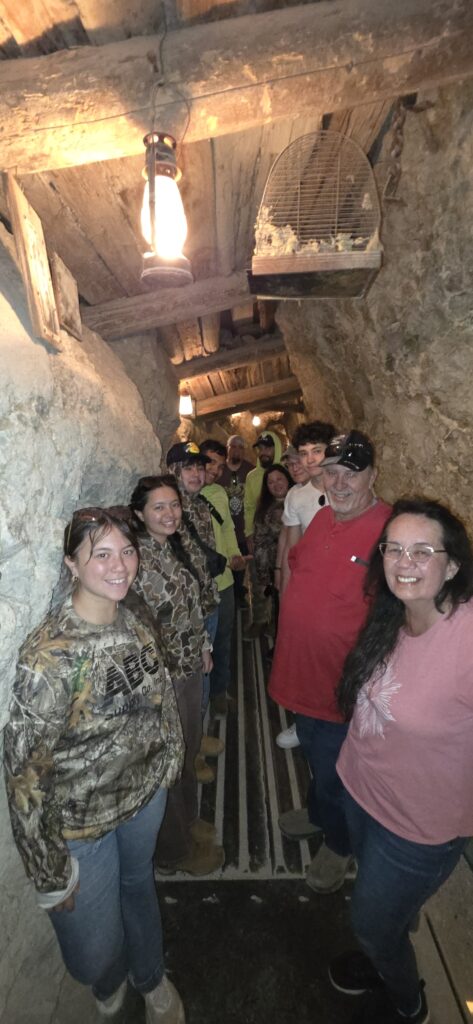 Smiling friends pose in a dim, rustic Nevada tunnel with stone walls during an ATV tour near the Colorado River, Las Vegas.