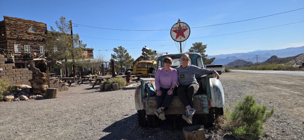 Two women relax on a vintage truck near Las Vegas in Nevada’s desert, beside a Texaco sign—perfect for ghost town sightseeing.
